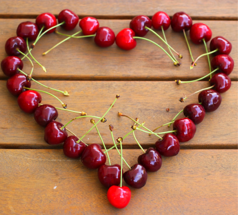 a photo of a heart outline made from cherries against a wooden background