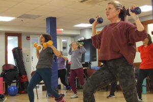 women in an exercise class lifting dumbbells while lunging forward